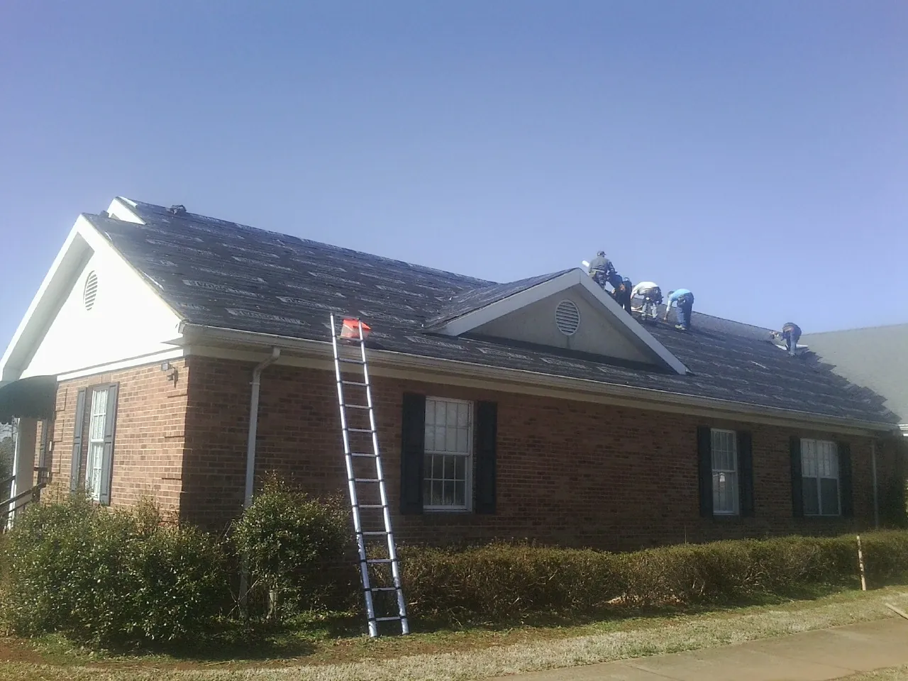 Crew tearing shingles off a brick ranch roof with a ladder set — Emergency Roof Repair work by our crew in Wyndmere