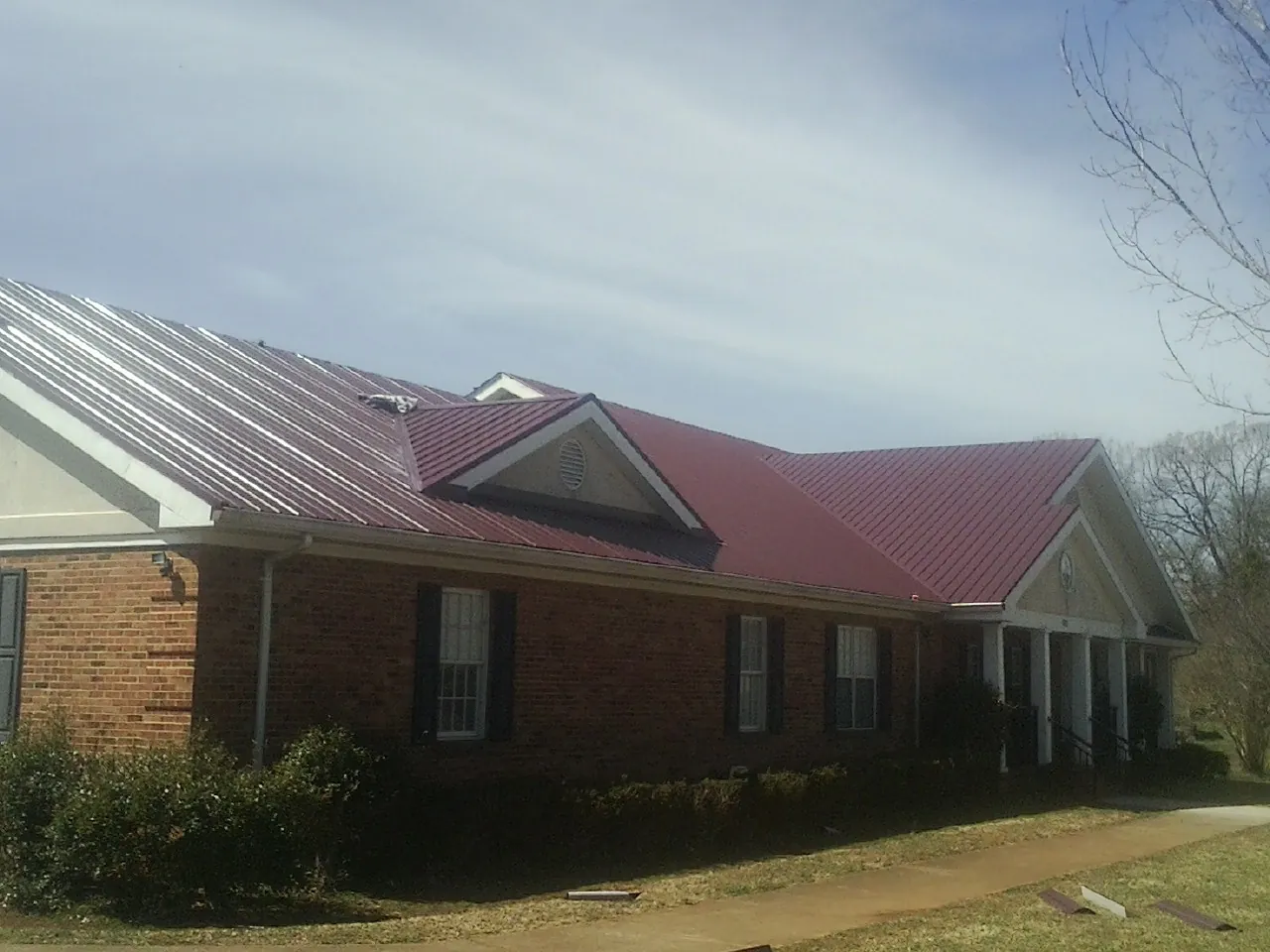 Red metal roof with gabled entries on a long brick building, from a Hail Damage Roof Repair job in Wyndmere