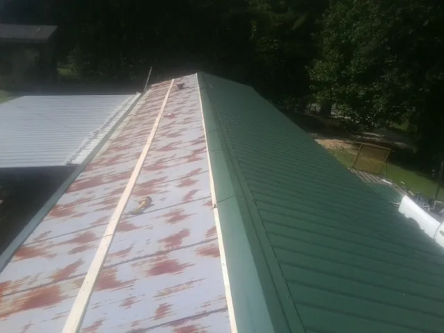 Old rusted panels beside newly installed green metal roofing — Wind Damage Roof Repair by Roofing Brothers in Wyndmere