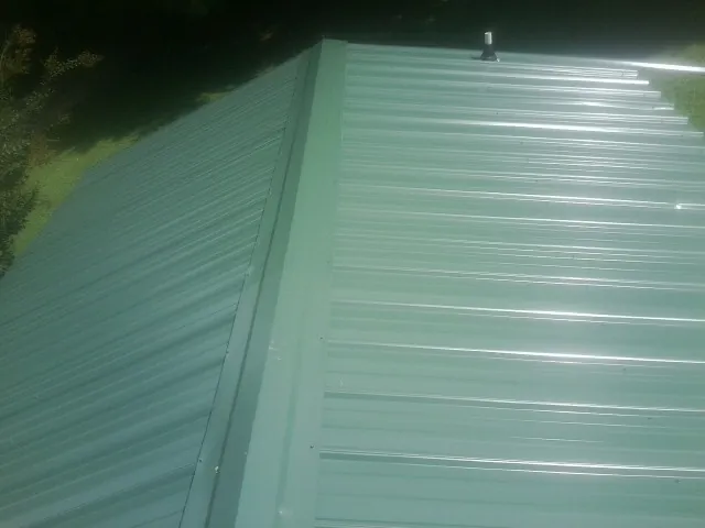 New green metal panels meeting at the ridge of a roof — Flat Roof Repair work by our crew in Wyndmere