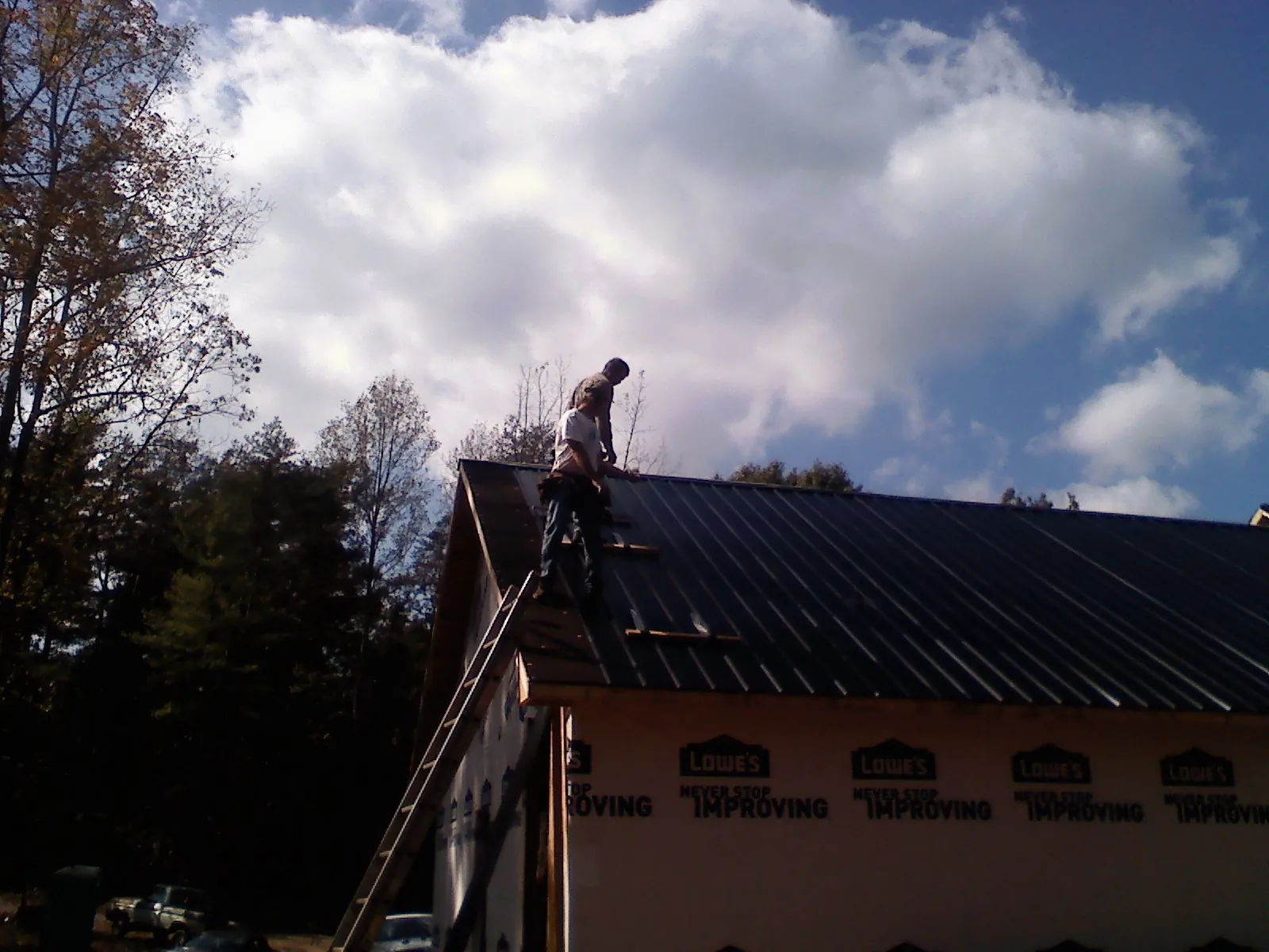 Roofer fastening dark metal panels high against a cloudy sky, from a Roof Inspection job in Wyndmere