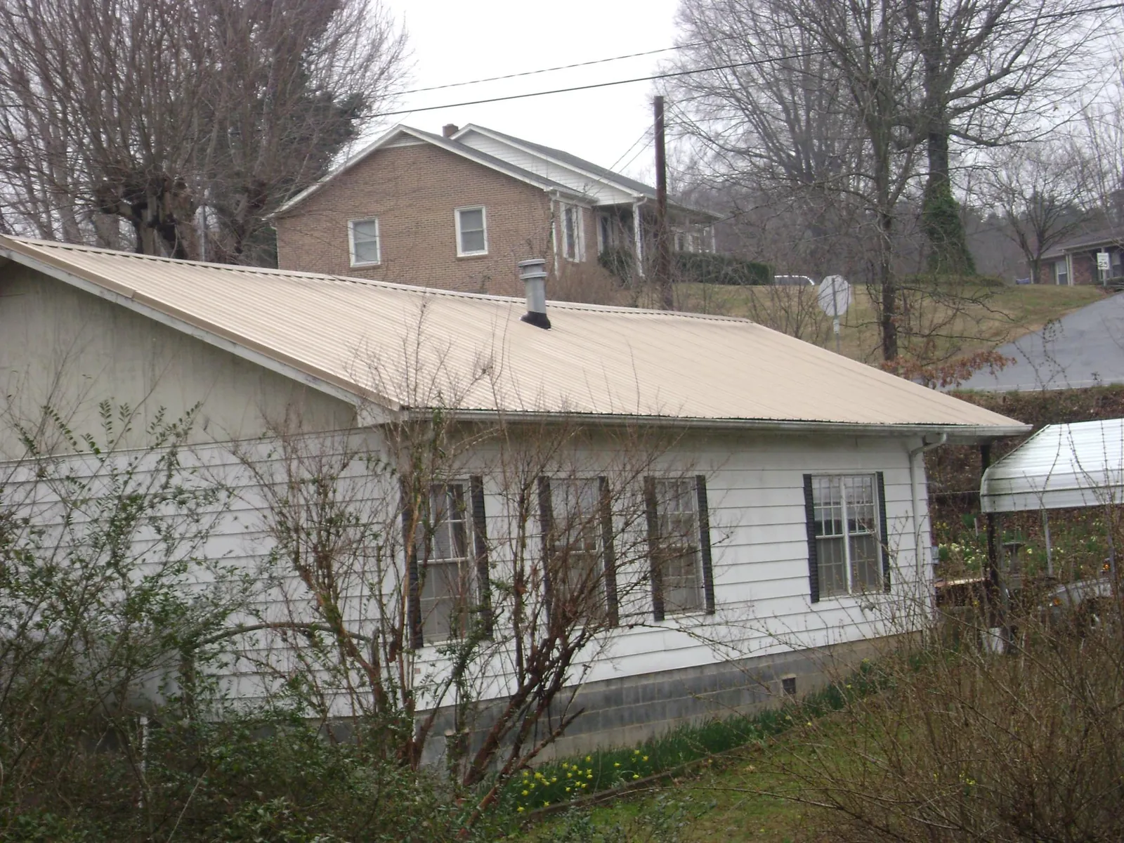 Tan metal roof on a white sided house set into a hillside — Commercial Roofing by Roofing Brothers in Wyndmere